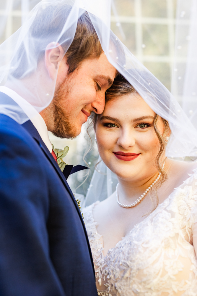 Bride and groom snuggled together underneath the bride's veil