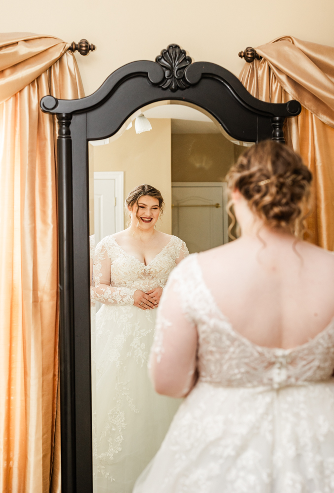 Bride gazing into the mirror and beaming with joy as she sees herself in her wedding dress on her wedding day.