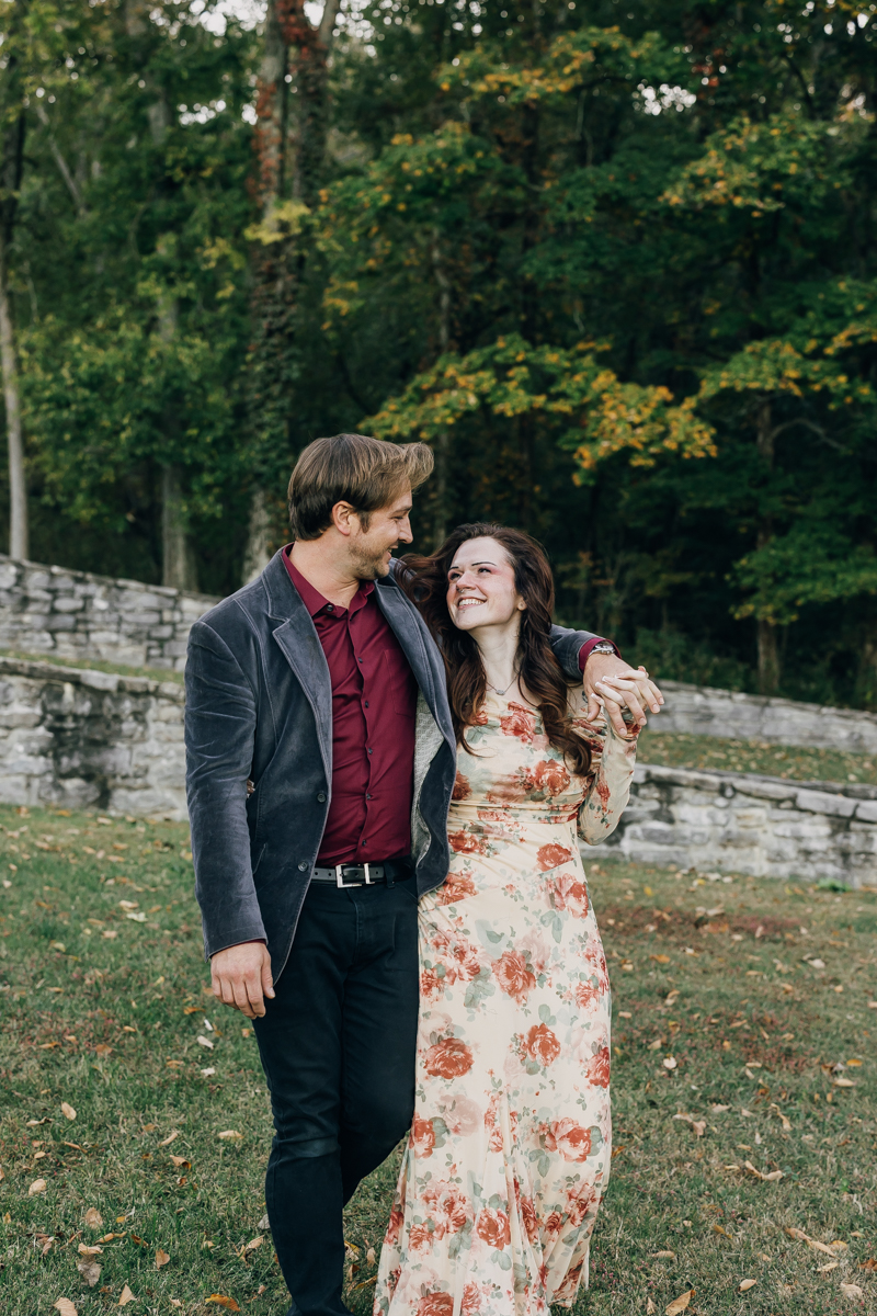 Engaged couple walking arm in arm and smiling at each other at Percy Warner Park in Nashville.