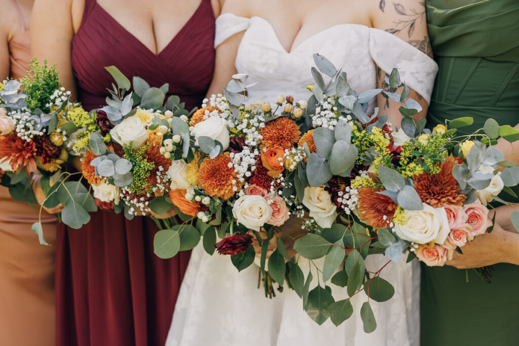 Bride and bridesmaids florals in shades of orange, burgundy, and cream