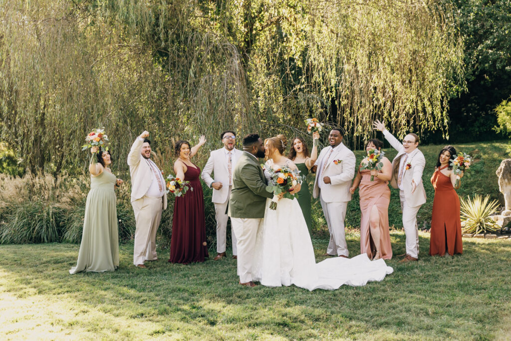 Wedding party cheering on the bride and groom while they share a celebratory kiss
