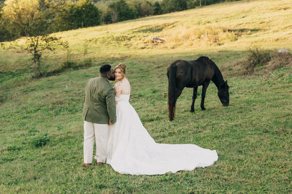 Groom kissing his bride on the cheek with a horse in the background