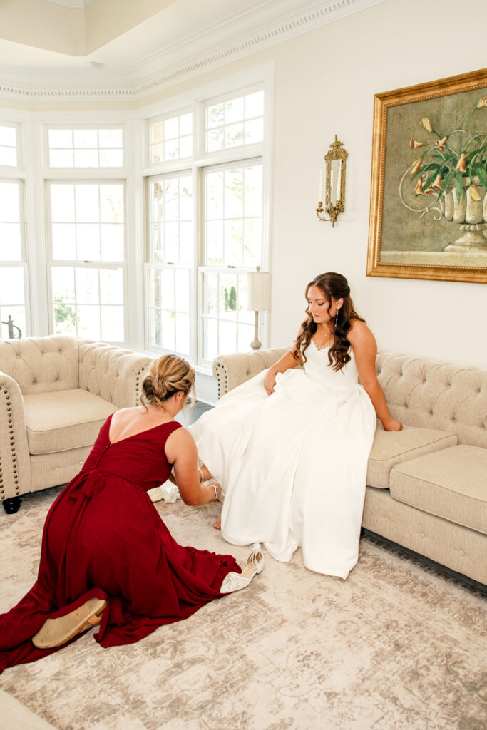 Maid of honor helping the bride into her shoes in the bridal suite at Stone Haven.