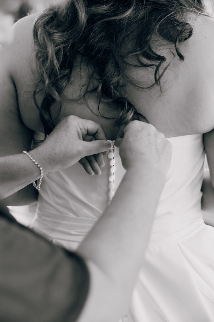 Close-up of the bride’s mother buttoning the back of her wedding dress.
