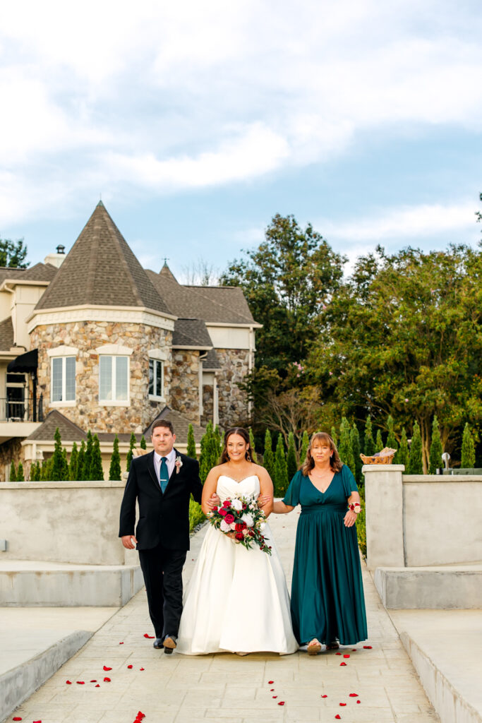 Bride walking down the aisle with her parents at an outdoor wedding ceremony on Stone Haven’s patio.
