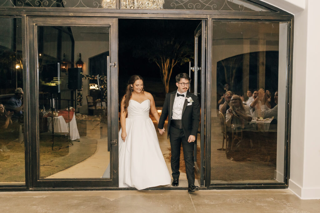 Bride and groom walking into their Stone Haven reception as guests cheer. 