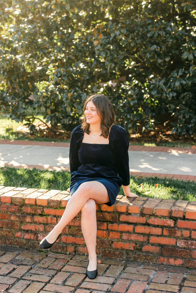 Senior sitting on brick wall with legs crossed, gazing into the distance.
