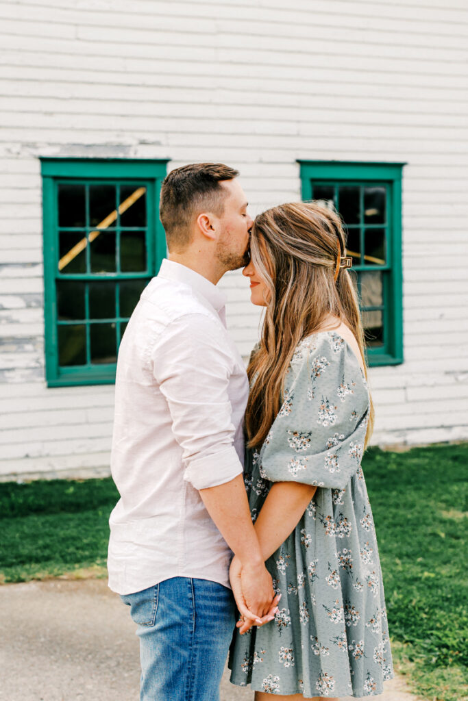 Man gently kissing his fiancé on the forehead while holding her hands