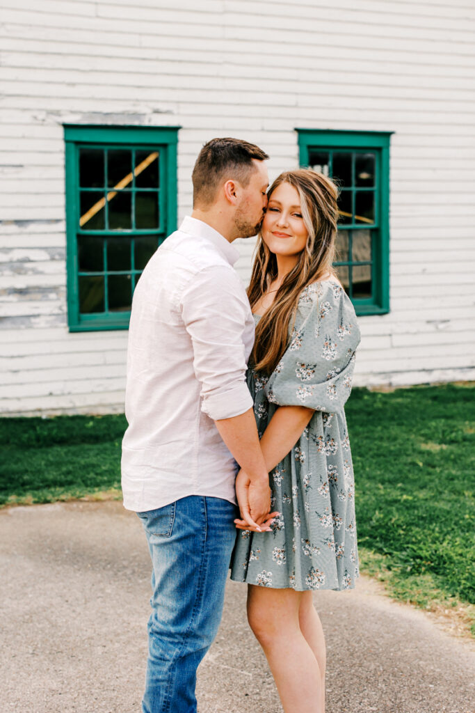 Man kissing his fiancée on the cheek while they hold hands