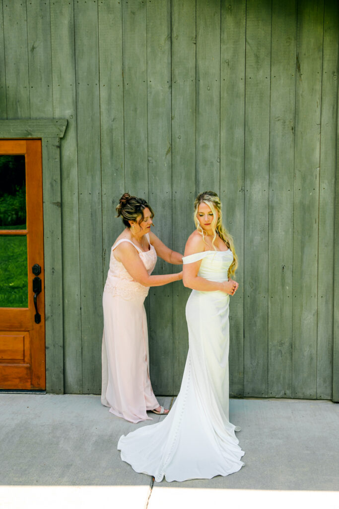 Mother of the bride fastening the back of her daughter’s wedding dress at 4 Points Farm