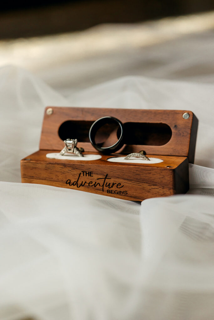 Wedding rings displayed in a wooden ring box engraved with “The adventure begins”