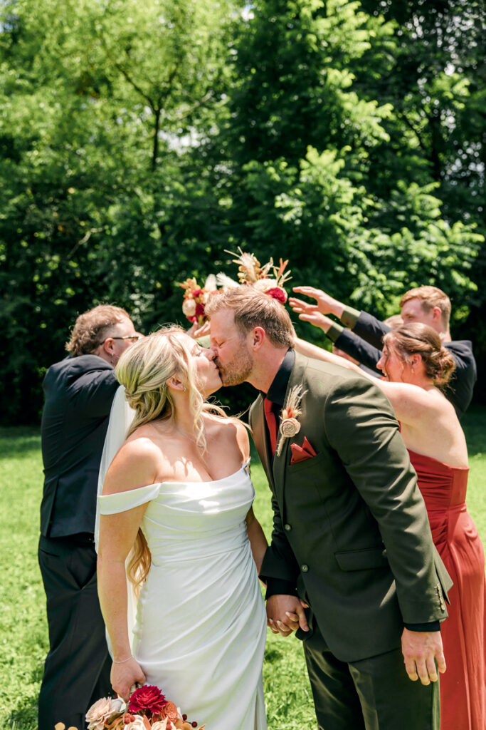 Bride and groom sharing a kiss with their wedding party in the background at 4 Points Farm