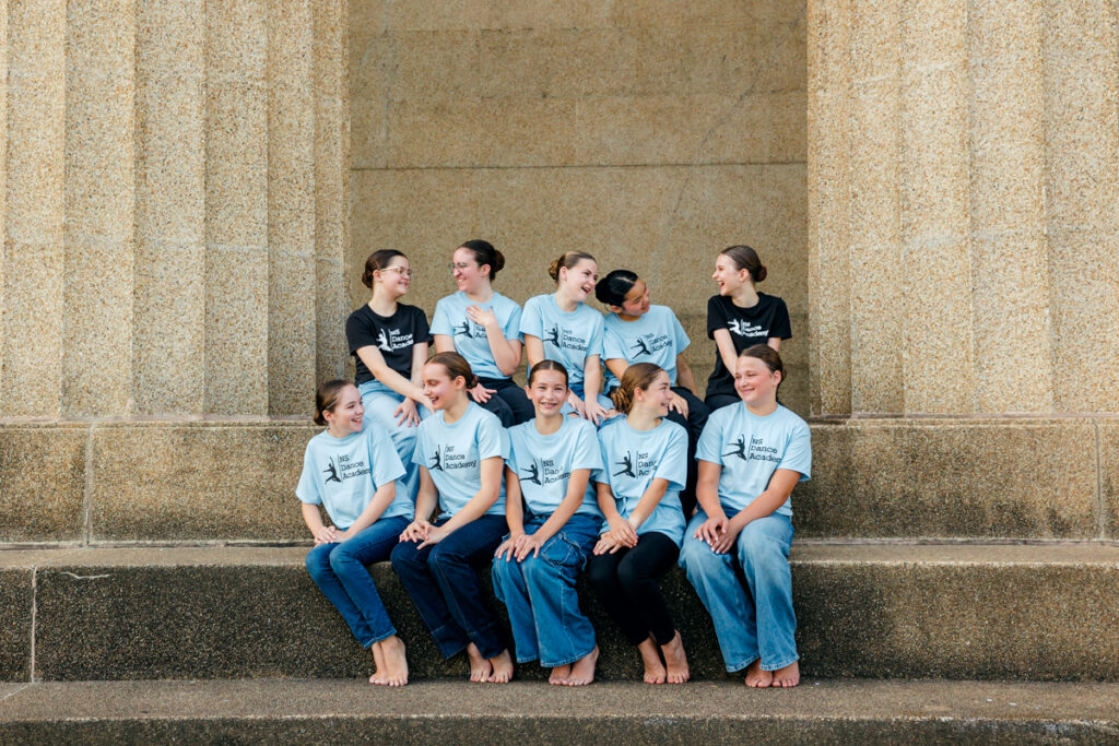 Outdoor portrait of ten young dancers laughing together on large steps.