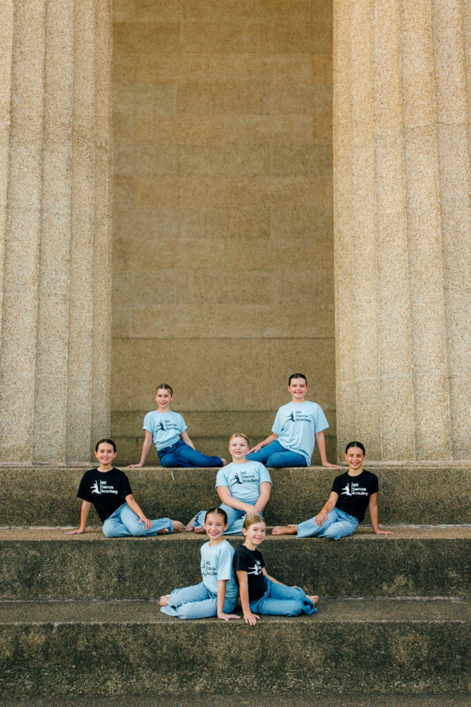 Seven dancers on steps in a side-sitting pose.