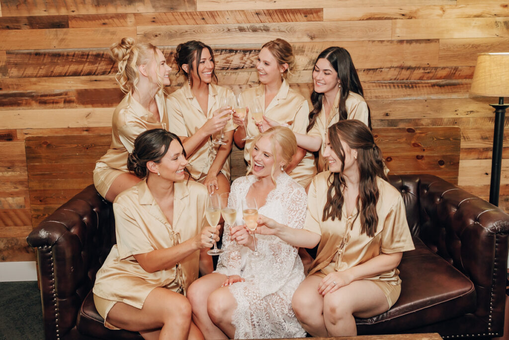 Bride and bridesmaids sitting on a couch and clinking their champagne glasses