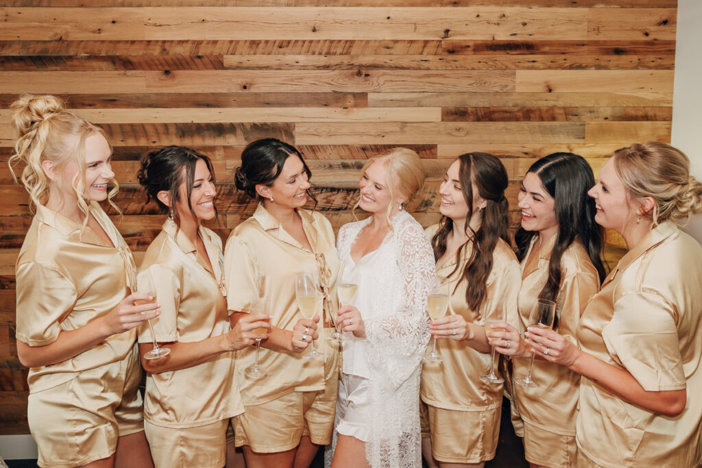 Candid moment of the bride and bridesmaids laughing and holding champagne glasses together