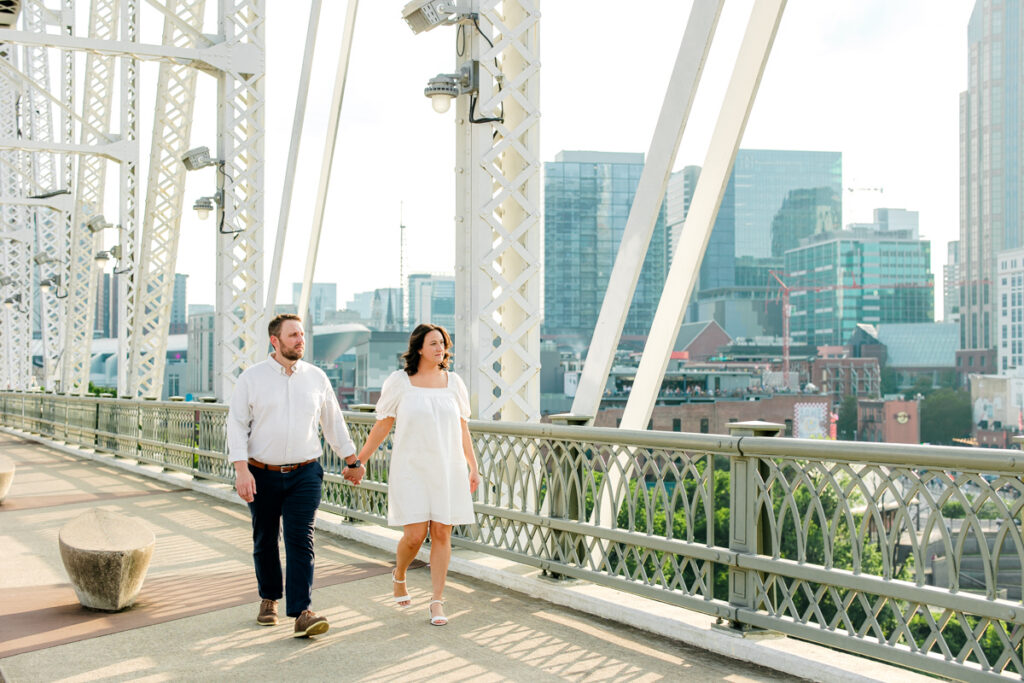 Engaged couple holding hands as they walk across the Pedestrian Bridge in Downtown Nashville