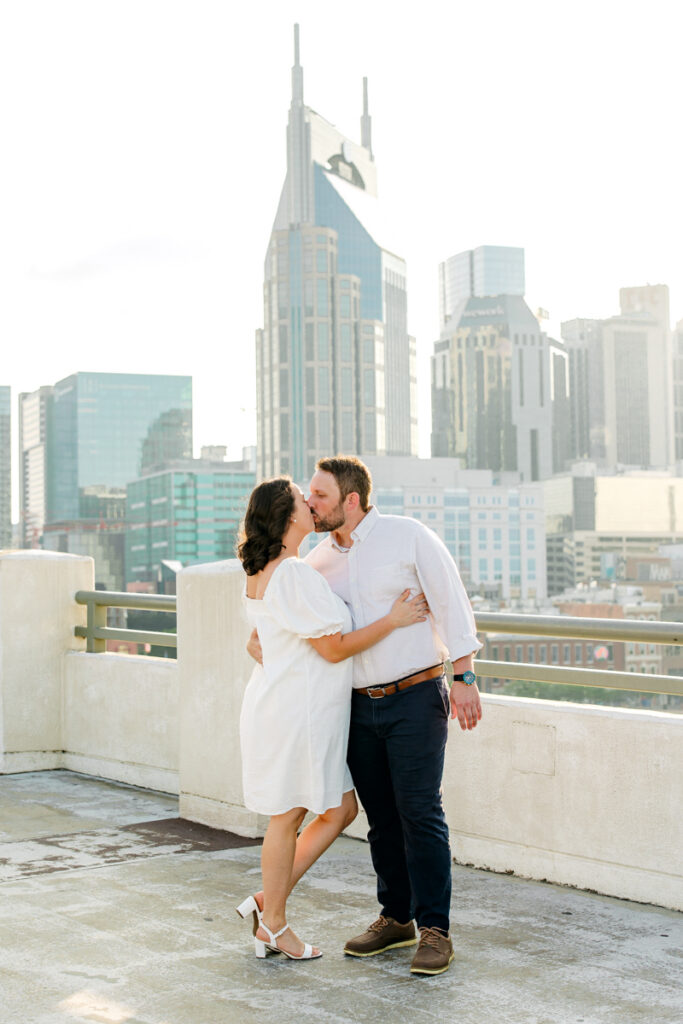 Engaged couple kissing with the Nashville skyline in the background