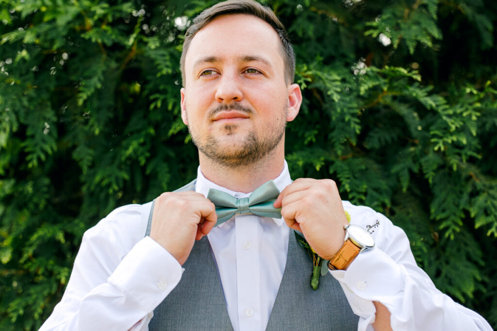 Groom adjusting his bowtie and gazing into the distance at Allenbrooke Farms