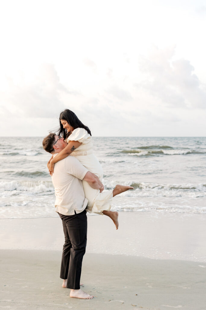 Man lifting his fianceé during their engagement session at Coligny Beach
